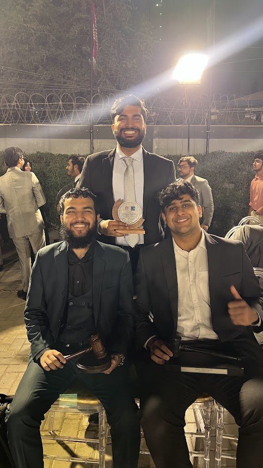 Three MUN Society Pakistan delegates with a Best Delegate trophy and gavels after a committee session.