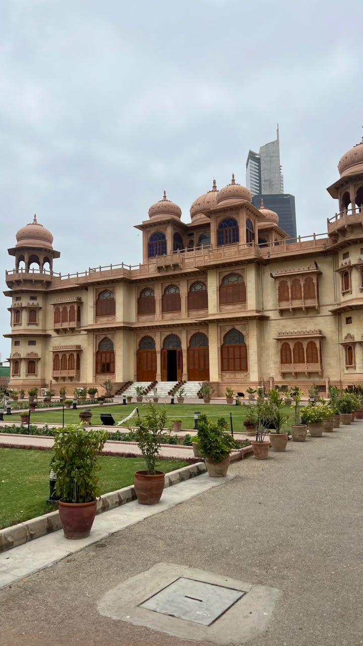 The pink stone front of Mohatta Palace in Karachi, with its domes and lawn, under an overcast sky.